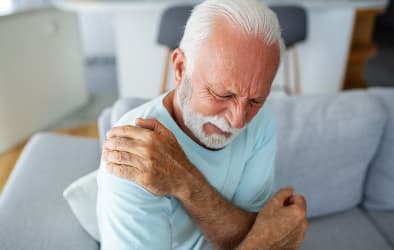 A picture of an older man holding his shoulder, suffering from muscle pain.
