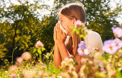 A picture of a woman covering her nose with a tissue while sitting in a green field.
