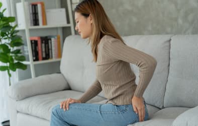 An image of a woman seated on a couch experiencing pain, likely due to piles.