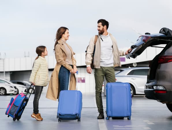 A picture of the family ready to go on the trip, standing by their car with luggage.