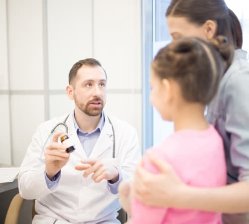 A picture of a doctor describing a kid and a lady about a medicine he holds in his hand.
